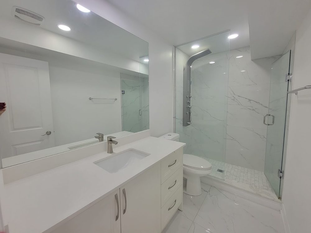 A basement bathroom with a white vanity, toilet and a glass shower