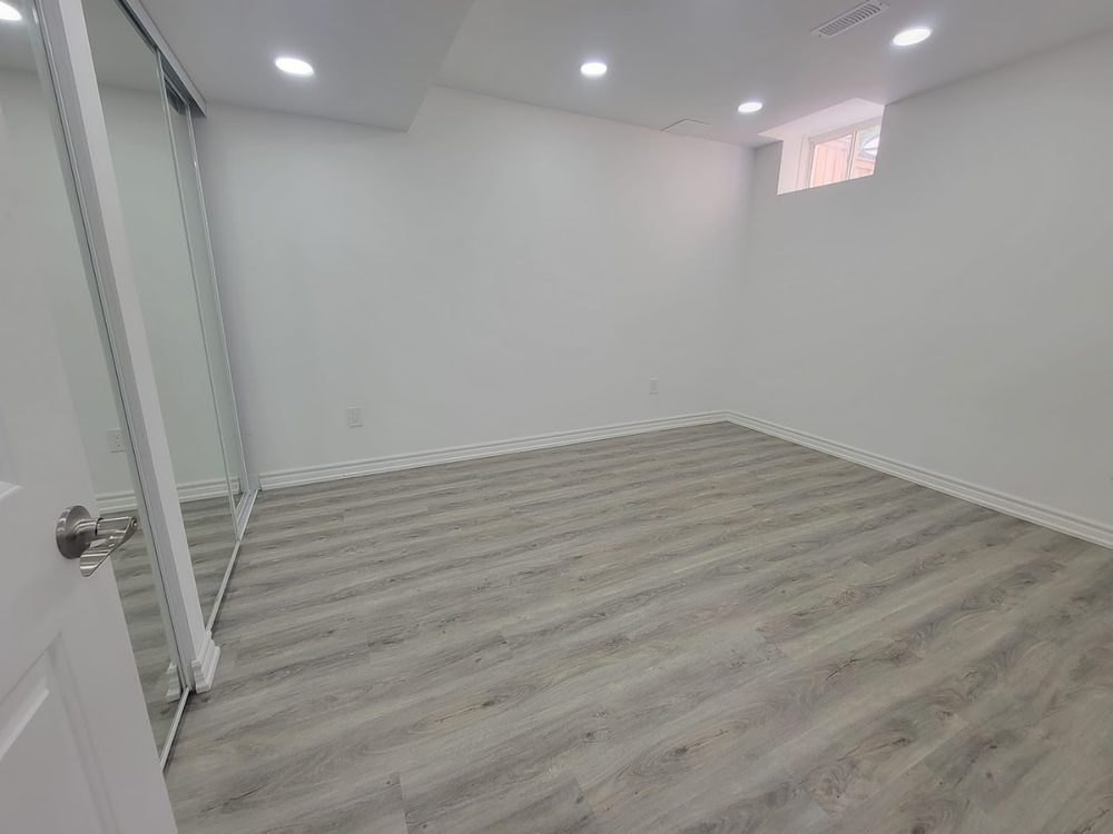 A finished basement bedroom with grey flooring and a mirrored closet