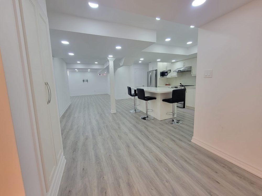 A bright finished basement with pot lights and grey plank flooring