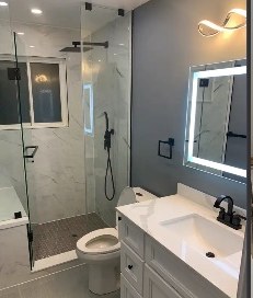 A finished bathroom by Tucasa: glass shower, marble-look tile, white vanity and a lit mirror