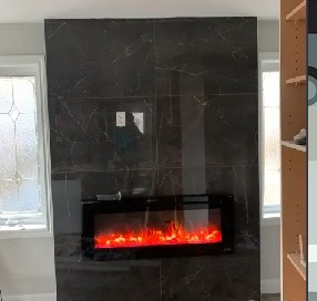 Finished feature wall in dark marble-look tile with an electric fireplace lit
