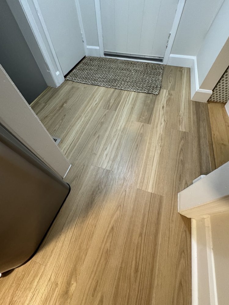 New plank flooring leading to an entry door with a woven mat