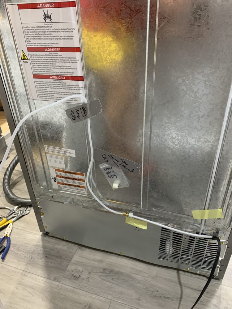 The back of a stainless fridge with the water line connected