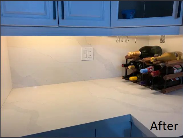 A white quartz counter and backsplash under blue upper cabinets with a wine rack
