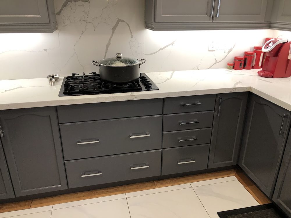 A gas cooktop on a white quartz counter above grey drawers