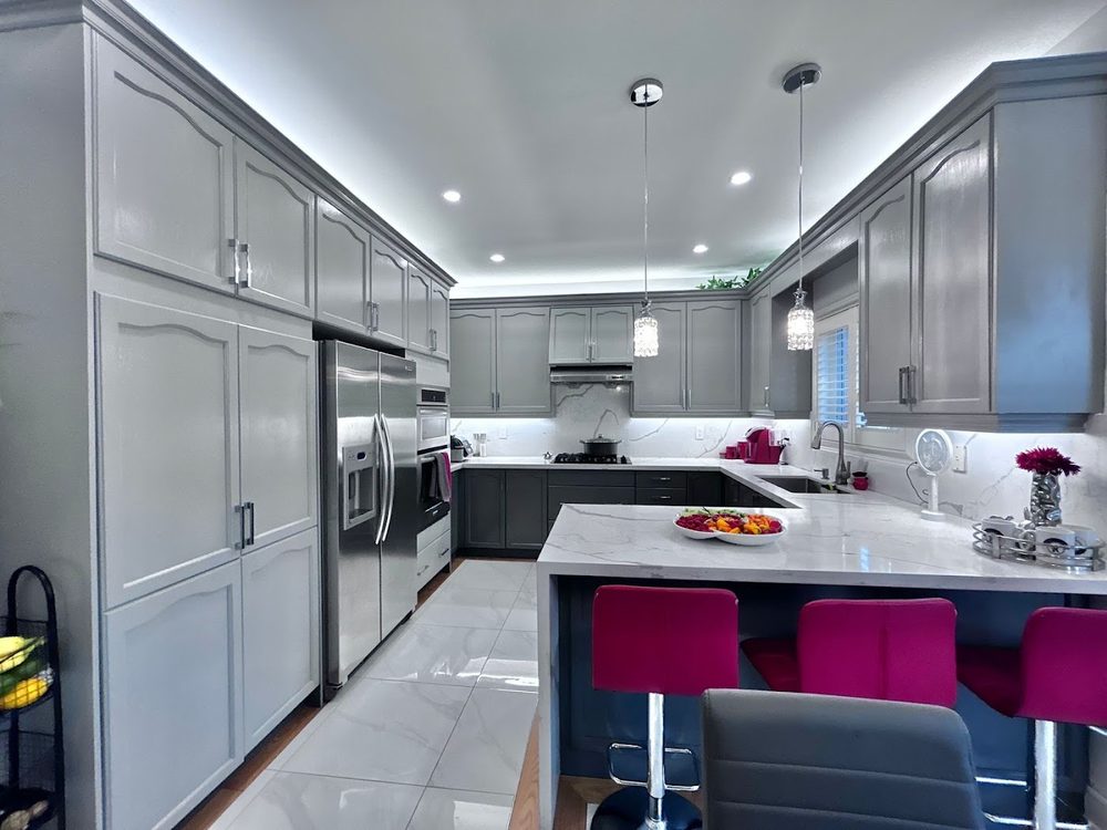 A large kitchen with grey cabinets, a white quartz counter and a stainless fridge