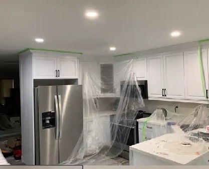 Kitchen mid-renovation with new white cabinets, pot lights and a stainless fridge