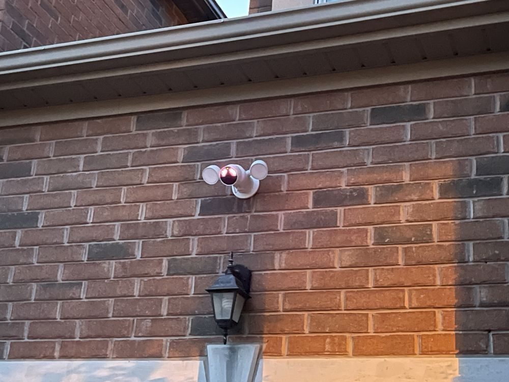 A security camera and black wall lantern on a red brick wall