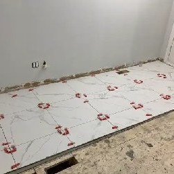 Large white marble-look floor tiles being laid with red levelling clips across a room