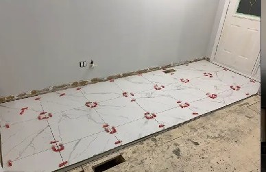 Large white floor tiles being laid with red levelling clips