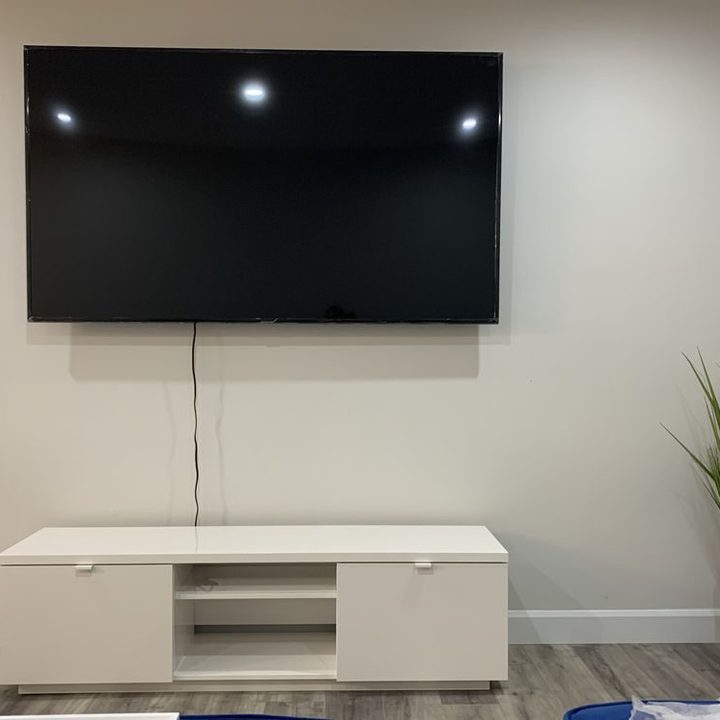 A flat-screen TV mounted on a living room wall above a white media unit