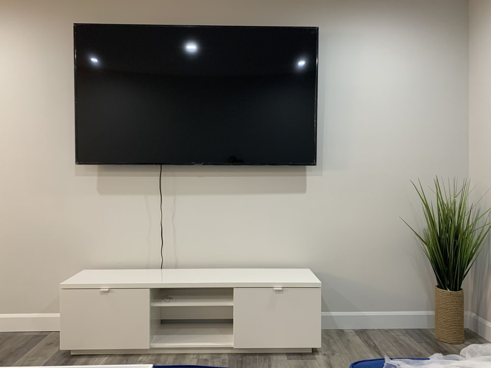 A wall-mounted TV above a white media unit with a plant